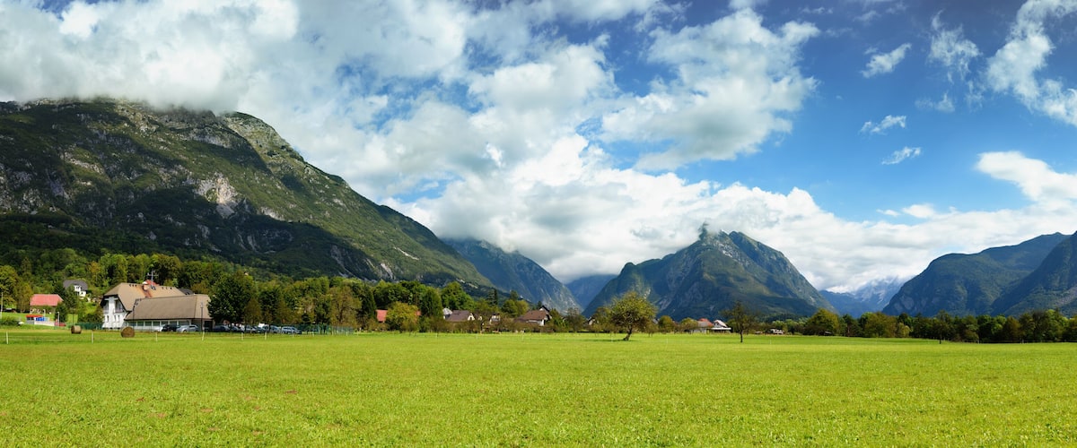 A mountainous landscape with a green field, houses, and a clear sky.