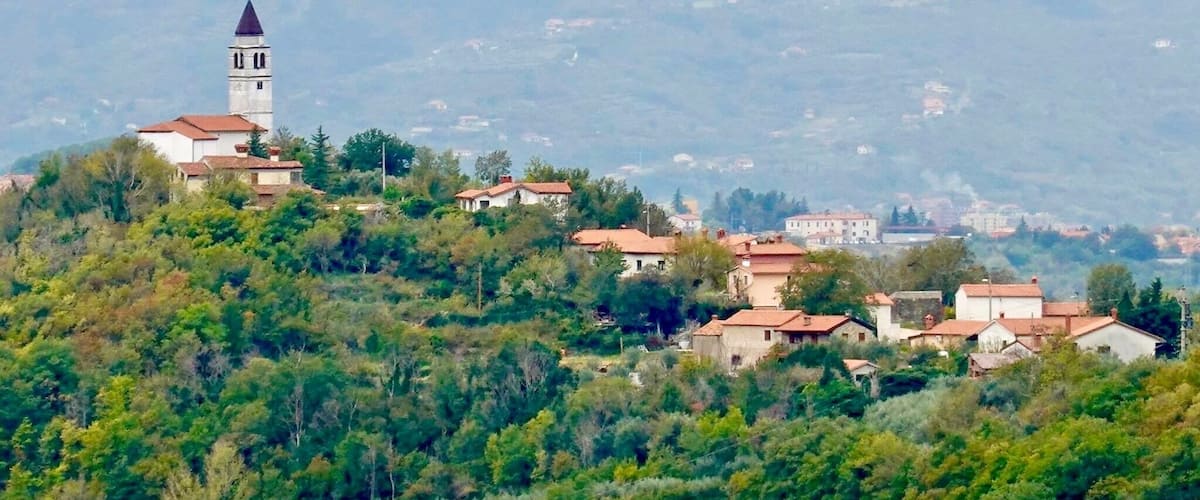 A village with a prominent church tower on a hill, surrounded by lush greenery and scattered houses.