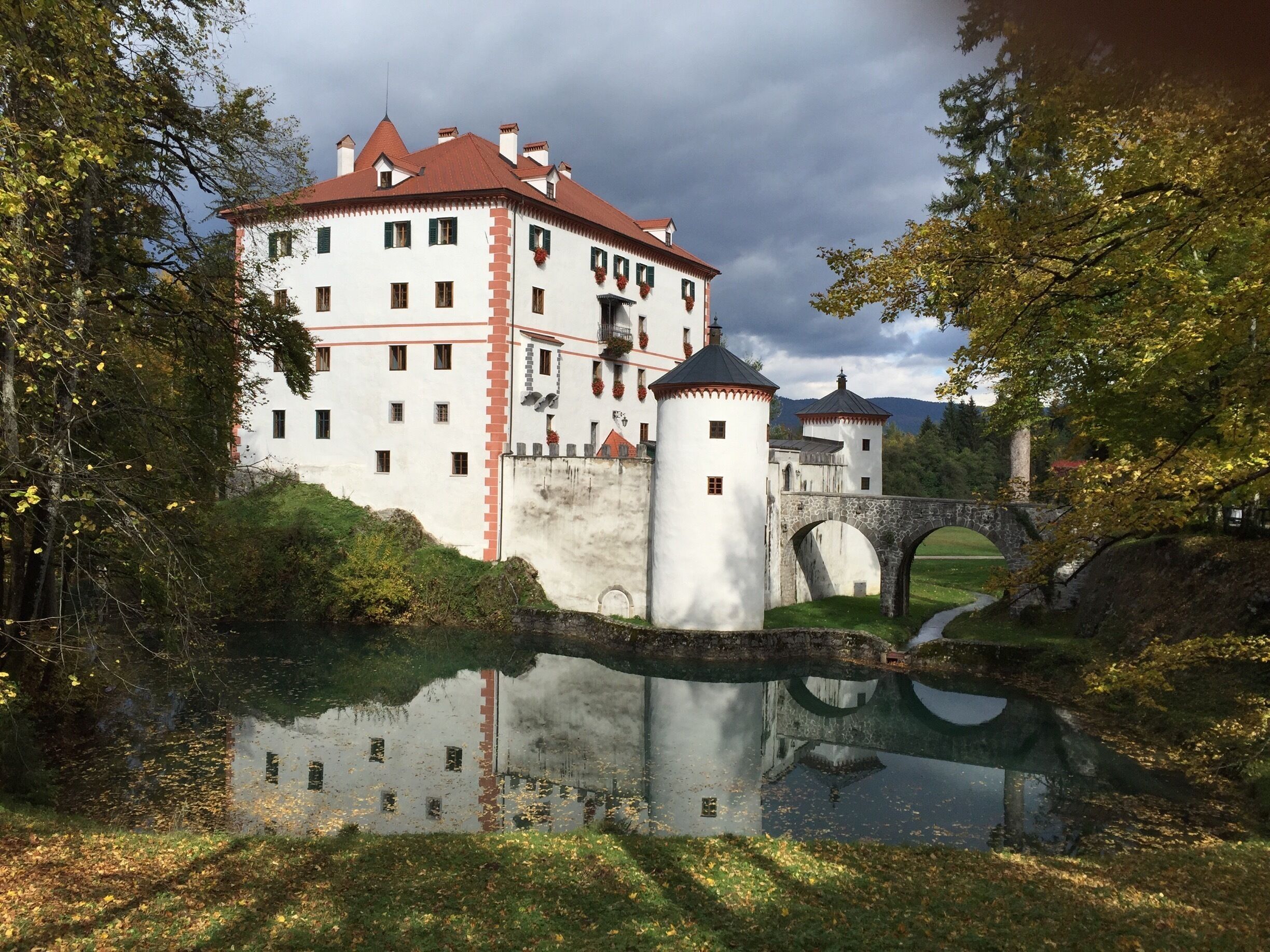 A castle with a moat, a bridge, and a reflection in the water.