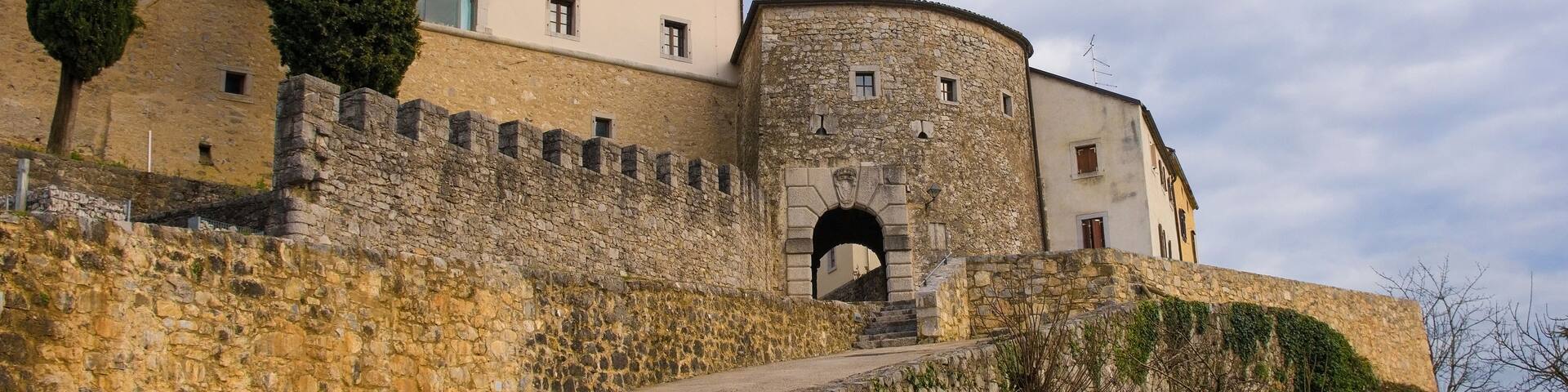 A historic stone building with a round tower, a paved pathway, and a stone wall.