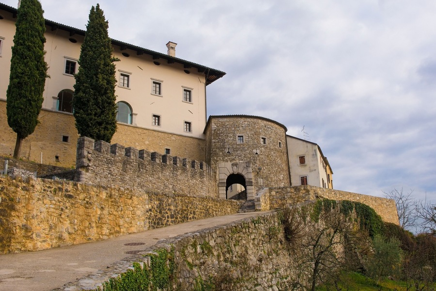 A historic stone building with a round tower, a paved pathway, and a stone wall.