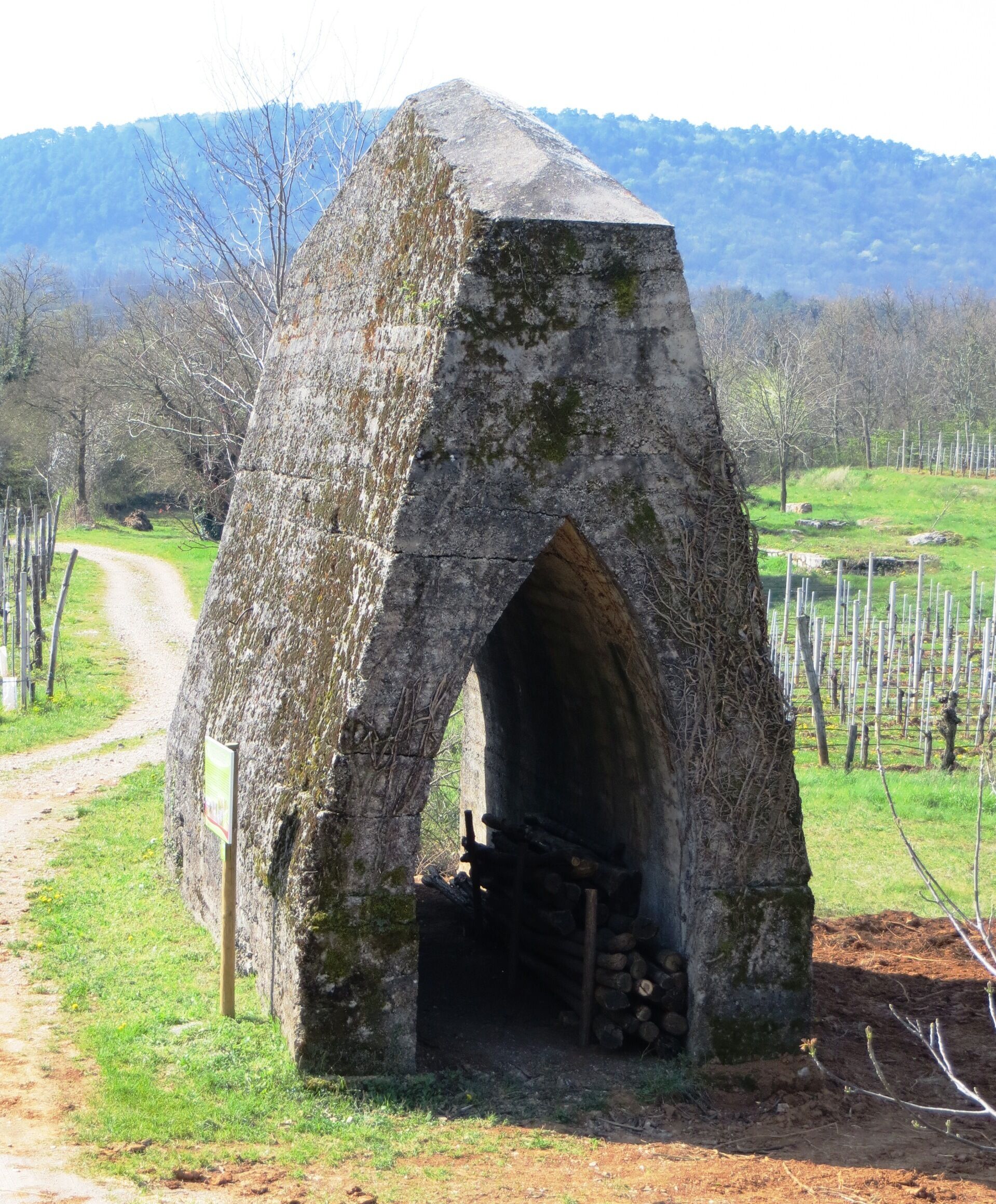 A stone structure with an archway, surrounded by a grassy area and a dirt path.