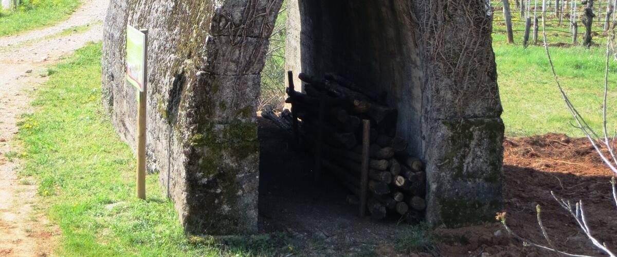 A stone structure with an archway, surrounded by a grassy area and a dirt path.