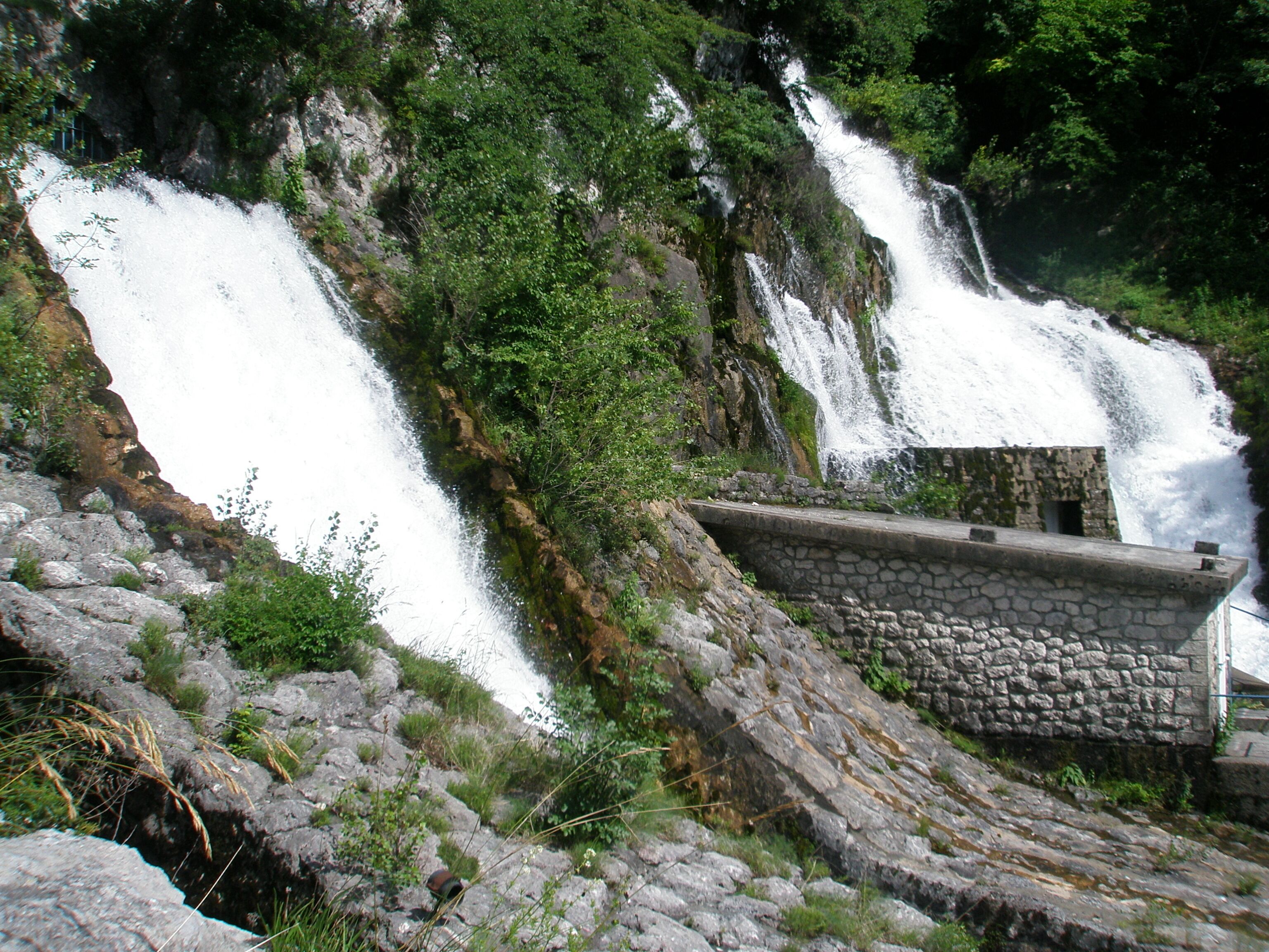 A waterfall cascading down a rocky slope with a stone structure at the base.