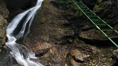 Uma cascata em área arborizada com uma ponte de corda.