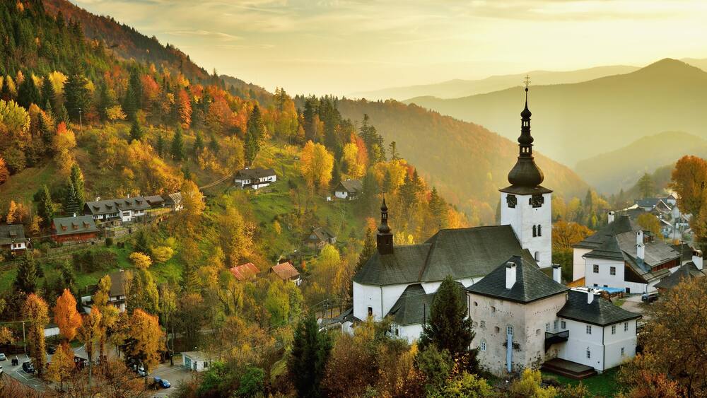 Fall in Slovakia. Old mining village. Historic church in Spania dolina. Autumn colored trees at sunset.