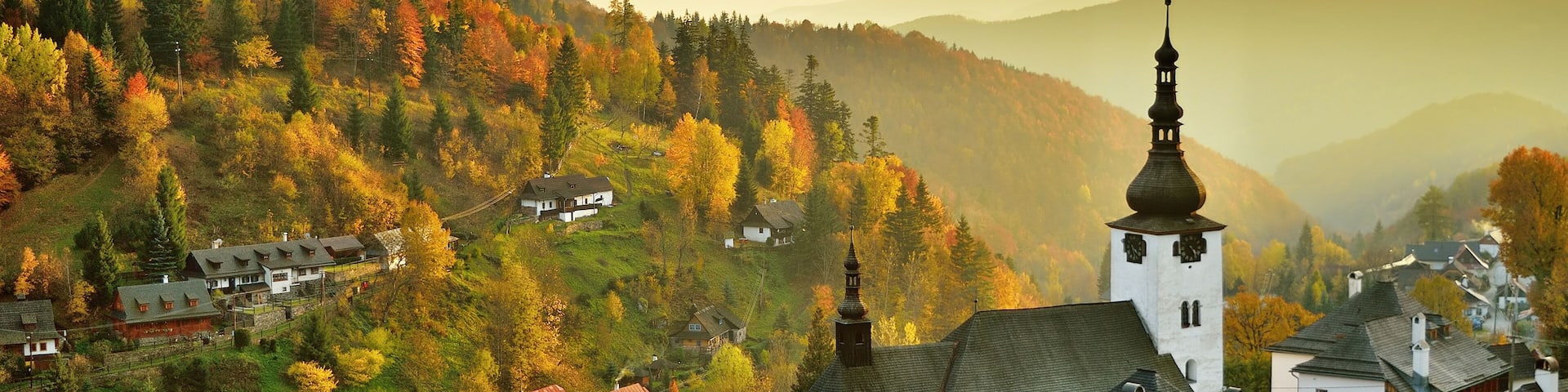 Fall in Slovakia. Old mining village. Historic church in Spania dolina. Autumn colored trees at sunset.