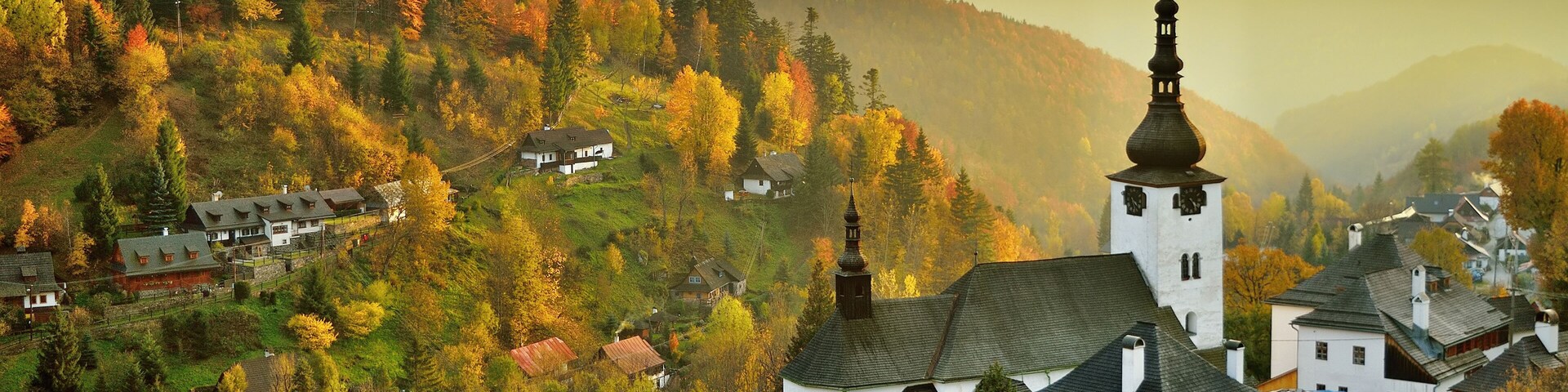 Fall in Slovakia. Old mining village. Historic church in Spania dolina. Autumn colored trees at sunset.