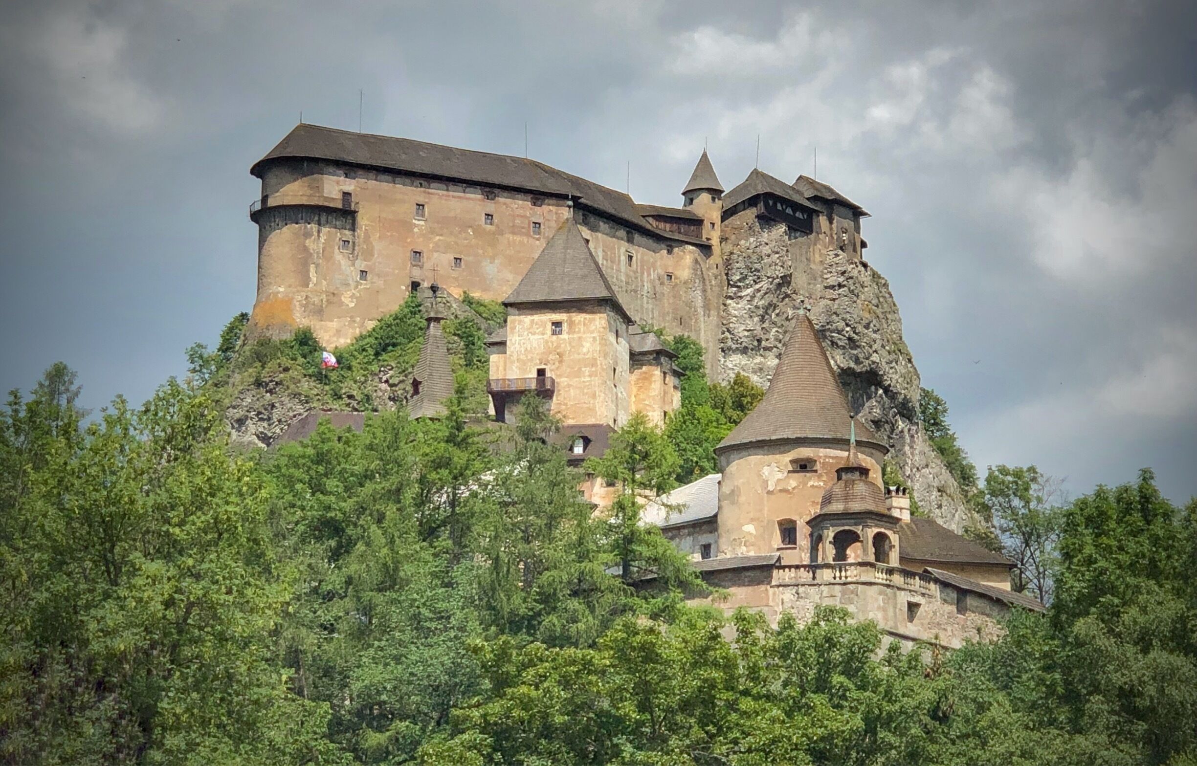 A historic castle perched on a rocky cliff, surrounded by lush greenery.