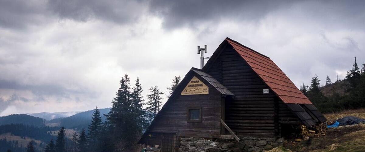 A wooden cabin with a steep roof, surrounded by a mountainous landscape and dense forest.
