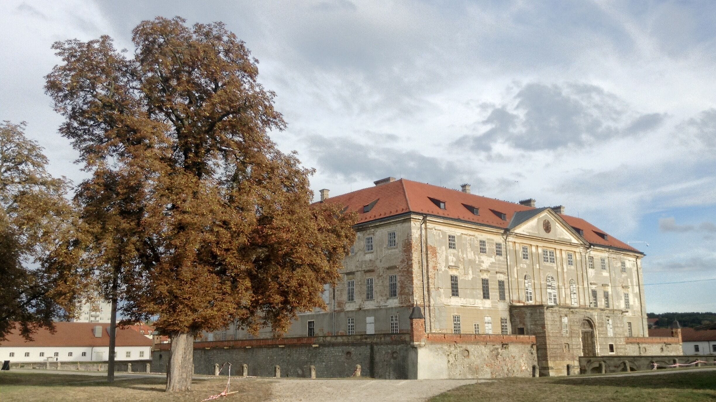 A large historic building with a red roof and a large tree in front.