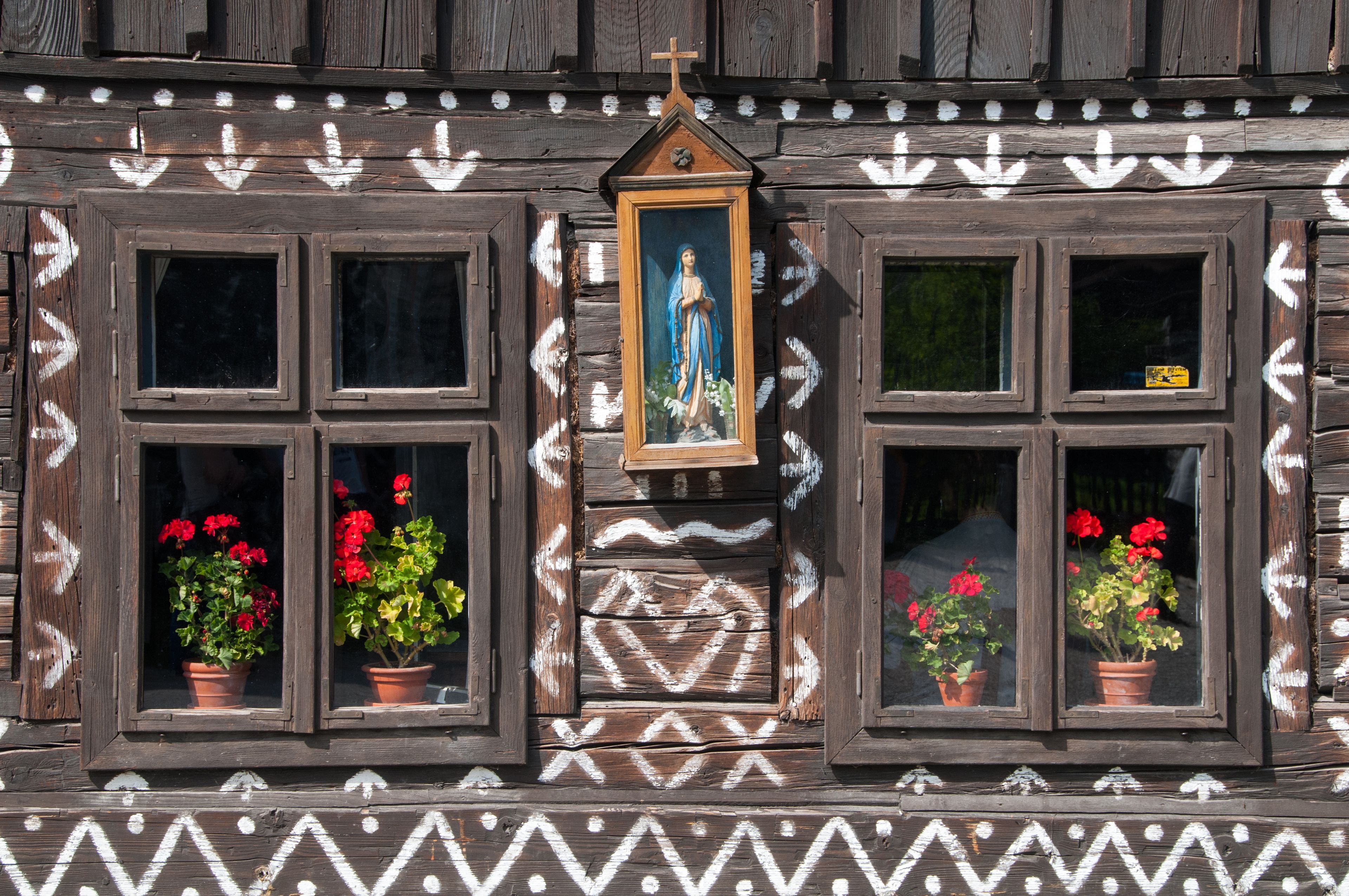 A wooden building with decorative patterns, a religious icon, and potted flowers.