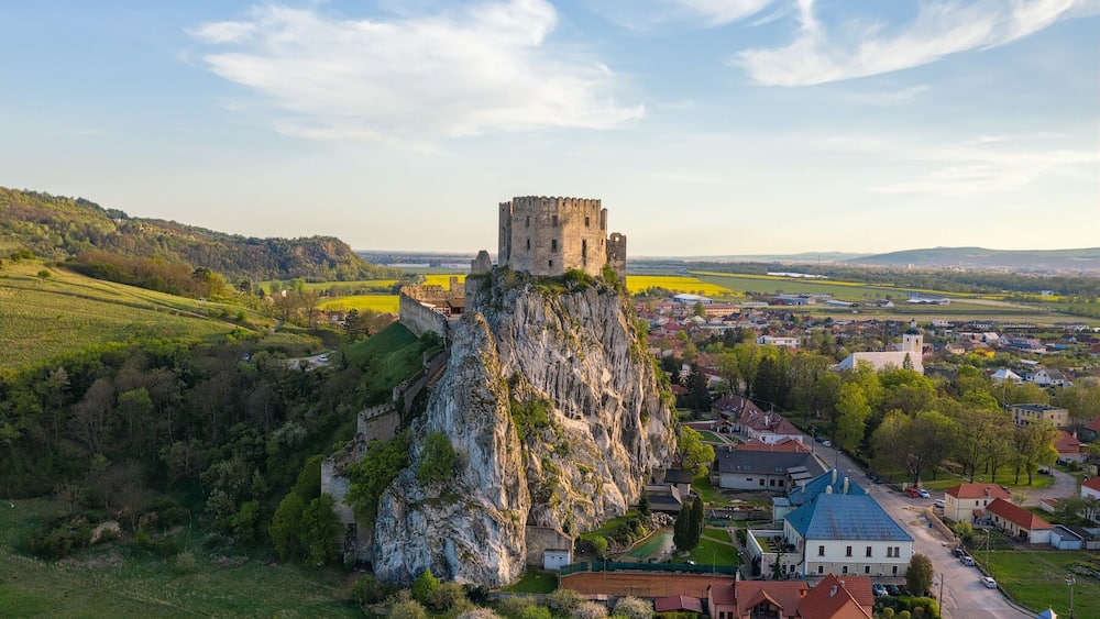 Eine Burg auf einem felsigen Hügel mit Blick auf eine Stadt mit Häusern und Feldern.