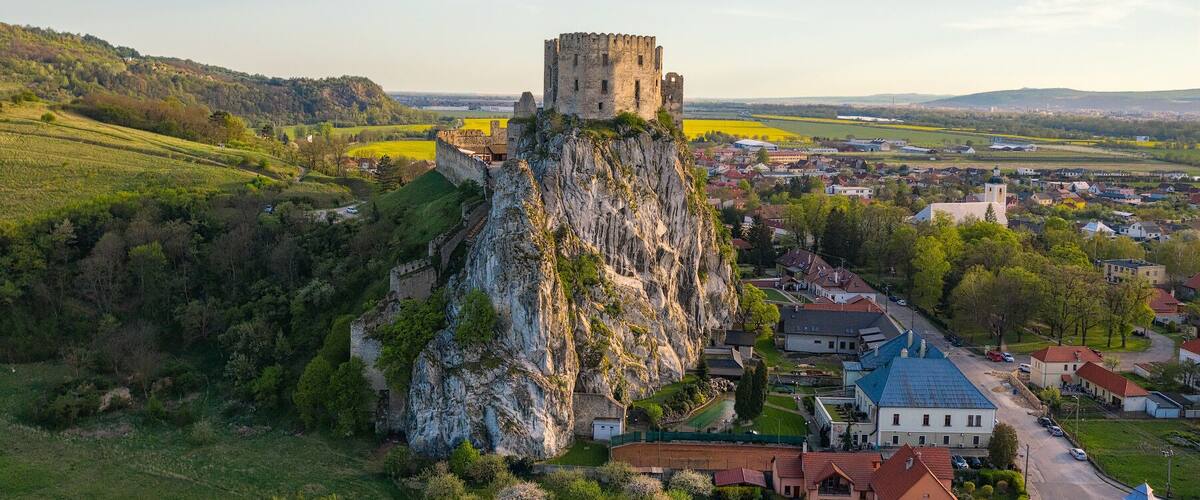 A castle atop a rocky hill overlooking a town with houses and fields.