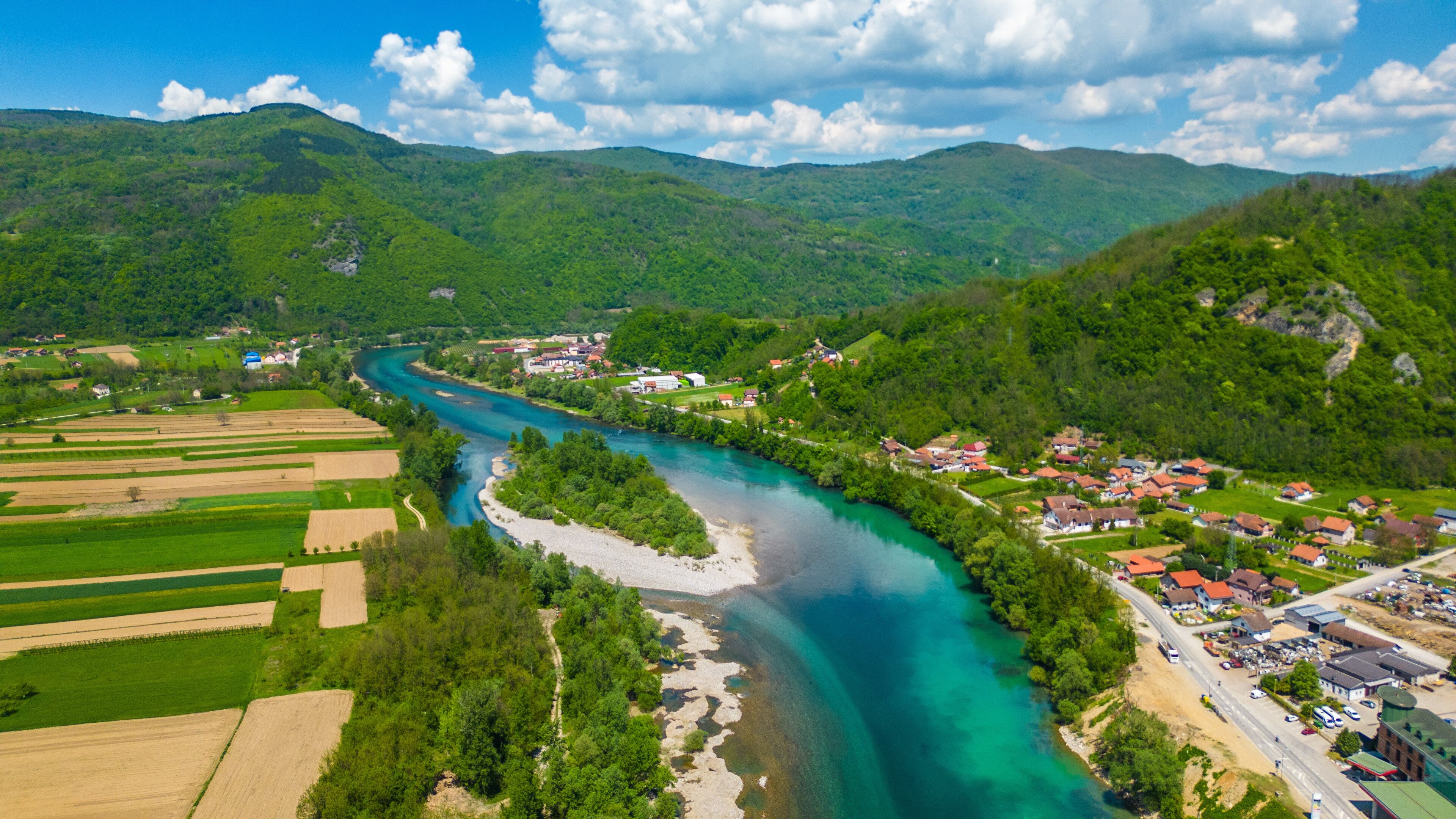 A river winding through a valley with green fields and a small village with red-roofed houses.