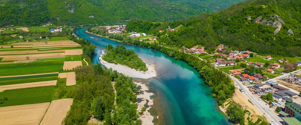 A river winding through a valley with green fields and a small village with red-roofed houses.