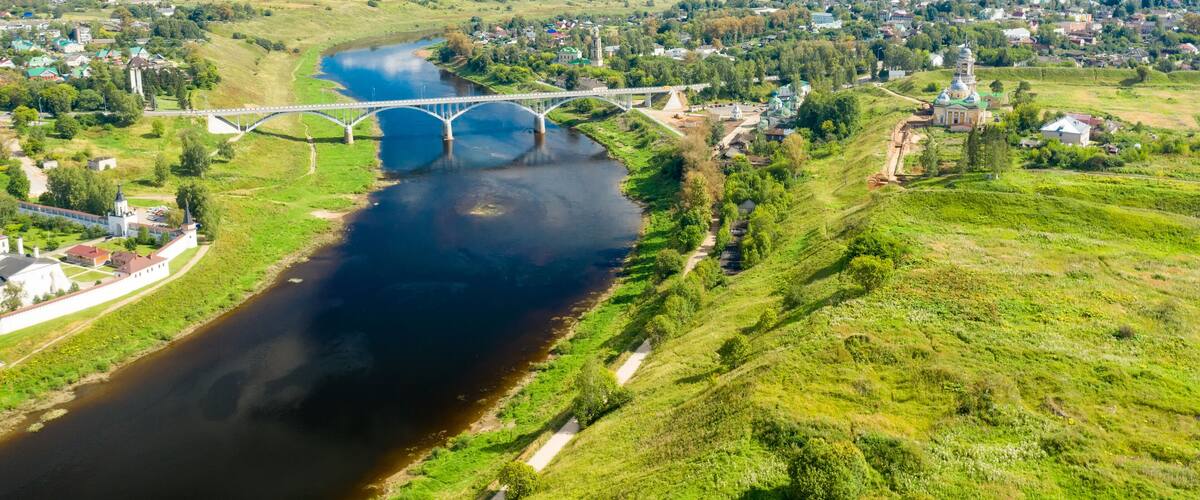 A river with a bridge, a town, and a large green hill.