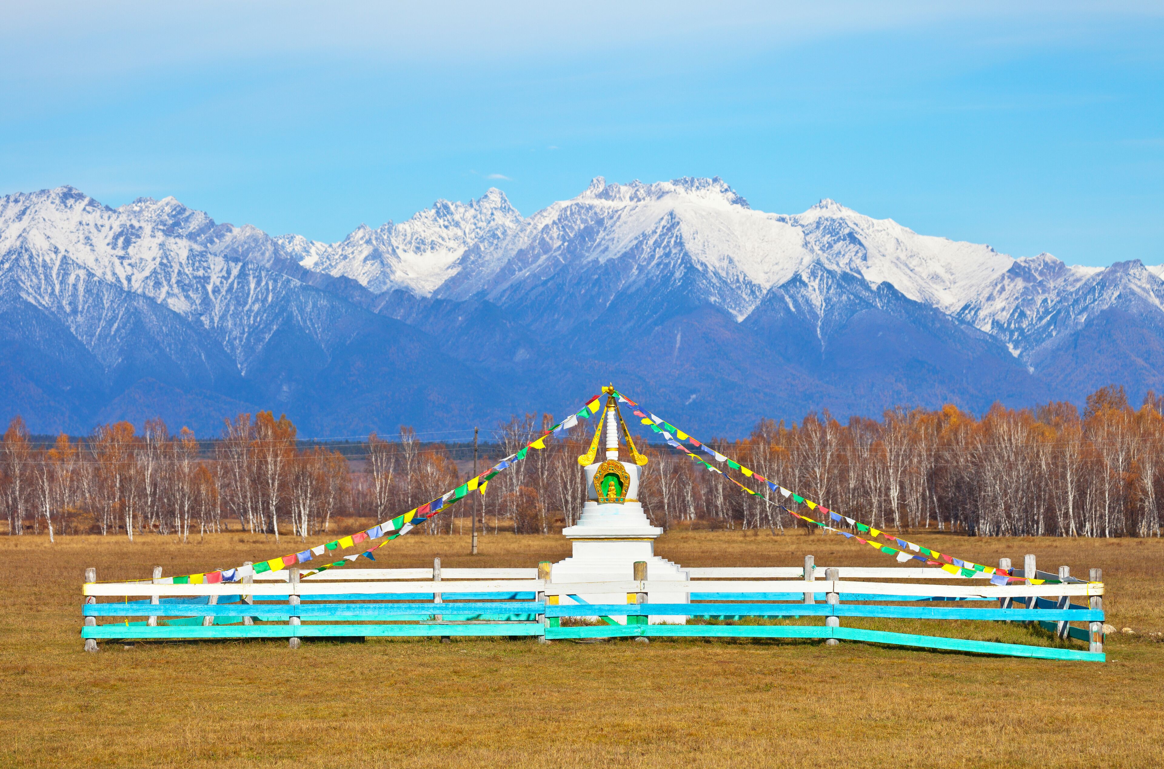 Buddhist stupa decorated with prayer flags against the background of snow-capped peaks of the Eastern Sayan Mountains on a sunny autumn day. Siberia. Baikal region. Buryatia. Tunka valley