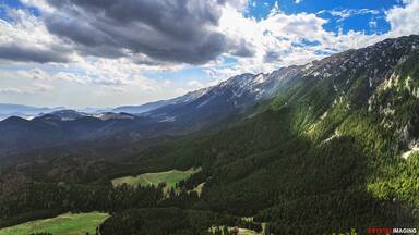 Un paisaje montañoso con un valle, bosques densos y un cielo despejado con nubes.