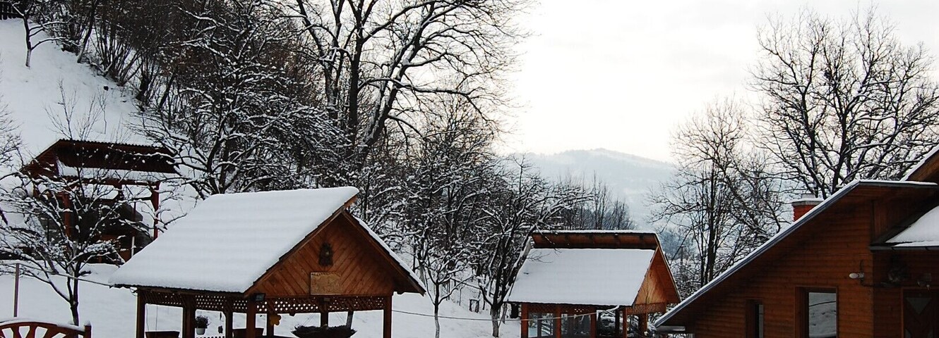 Un espacio exterior cubierto de nieve con cabañas de madera, un pabellón de madera y un pequeño estanque.