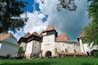 Un château historique doté de nombreuses tours et d’une façade blanche, entouré d’une végétation luxuriante et surplombé d’un ciel partiellement nuageux.