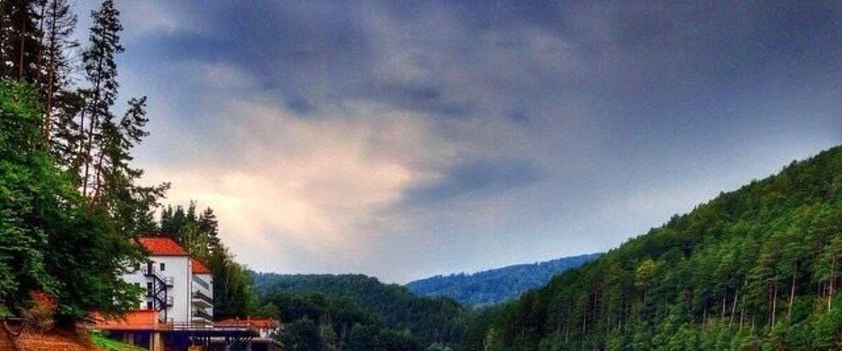 A calm lake with a house on the left and a forested hillside on the right.