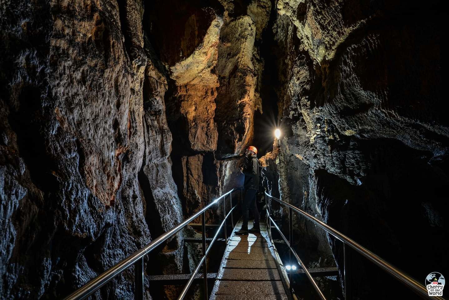 A person standing on a metal staircase inside a cave with rough rock walls and a light source at the top.