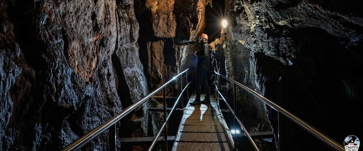 A person standing on a metal staircase inside a cave with rough rock walls and a light source at the top.