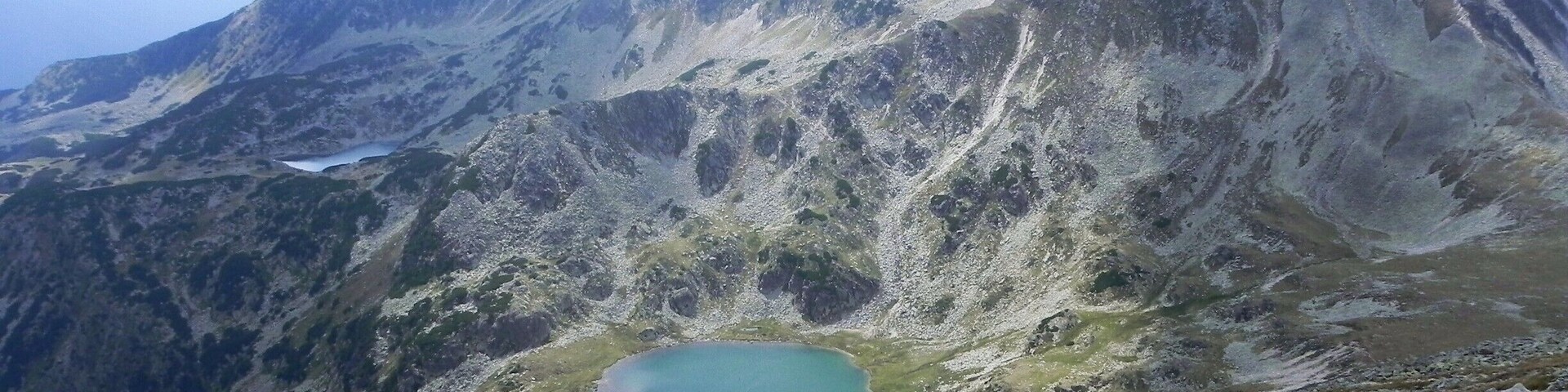 Paisaje montañoso con un lago pequeño rodeado de terreno rocoso.
