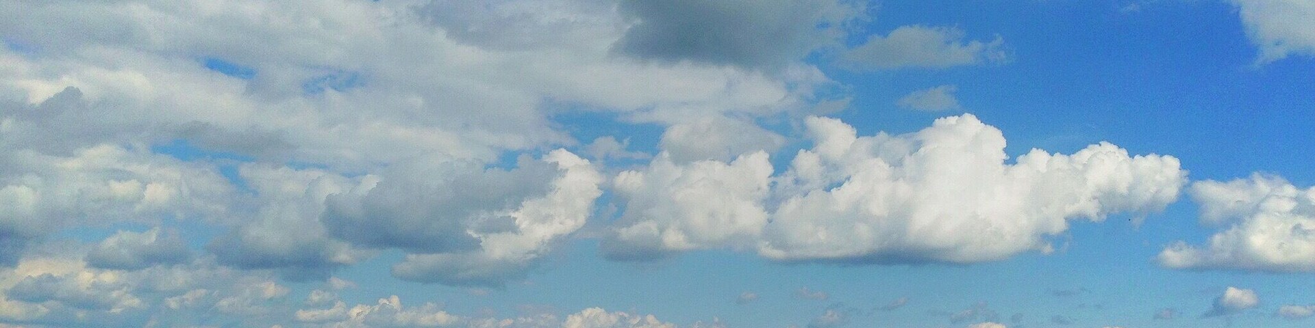 Colinas ondulantes, un cielo despejado con nubes y una cadena montañosa distante.
