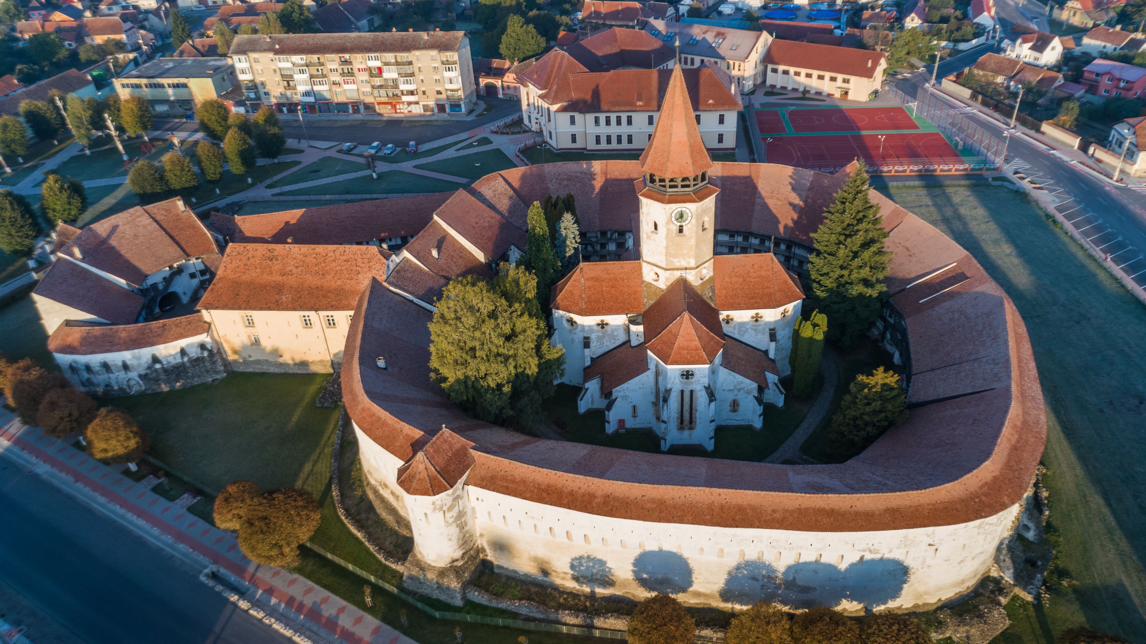 Oversigtsbillede af en historisk by omgivet af mure, med en markant kirke med et højt spir, samt boliger og en sportsplads.