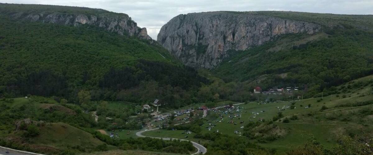 A valley with steep cliffs, a winding road, and scattered buildings.