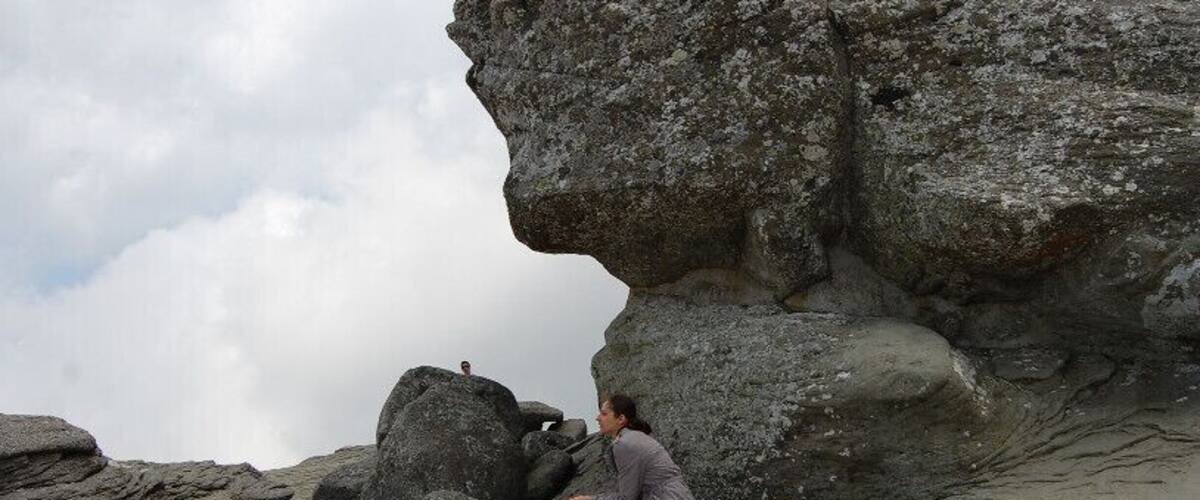 A rocky landscape with a large boulder formation and a person climbing.