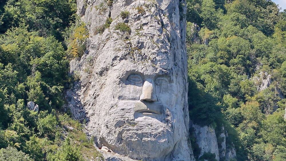 Decebalus is considered a national hero in Romania and has been portrayed in numerous literary works, movies, public sculptures, and other memorials.
The rock sculpture of Decebalus (Romanian: Chipul regelui dac Decebal) is a 42.9 m (141 ft) in height and 31.6 m (104 ft) in width carving in rock of the face of Decebalus (r. AD 87–106), the last king of Dacia, who fought against the Roman emperors Domitian and Trajan to preserve the independence of his country, which corresponded to modern Romania.
The sculpture was made between 1994 and 2004, on a rocky outcrop on the river Danube, at the Iron Gates, which form the border between Romania and Serbia. It is located near the city of Orșova in Romania.
It is the tallest rock relief in Europe.
The project of sculpting the colossal head of Decebalus was the brainchild of a wealthy Romanian businessman, Iosif Constantin Drăgan. In 1985, Drăgan chose the rock to be sculpted, an outcrop 128m in height located in the area of Iron Gorge, Danube. Perhaps one of the reasons Drăgan chose this site was due to the fact that the Tabula Traiana, a memorial to the Roman conquest of Dacia, was located on the opposite side of the river.
After the sculpture was completed Latin inscription was put beneath it and is: DECEBALUS REX DRAGAN FECIT, which meant “King Decebalus, made by Dragan”.
The best photographs are made while cruising if you are visiting from serbian side or from a bridge if you are already in Romania.
#InStone
#History
#Romania
#Serbia
#Danube