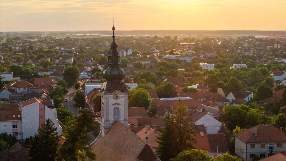 A town with a prominent church tower and a river in the background.