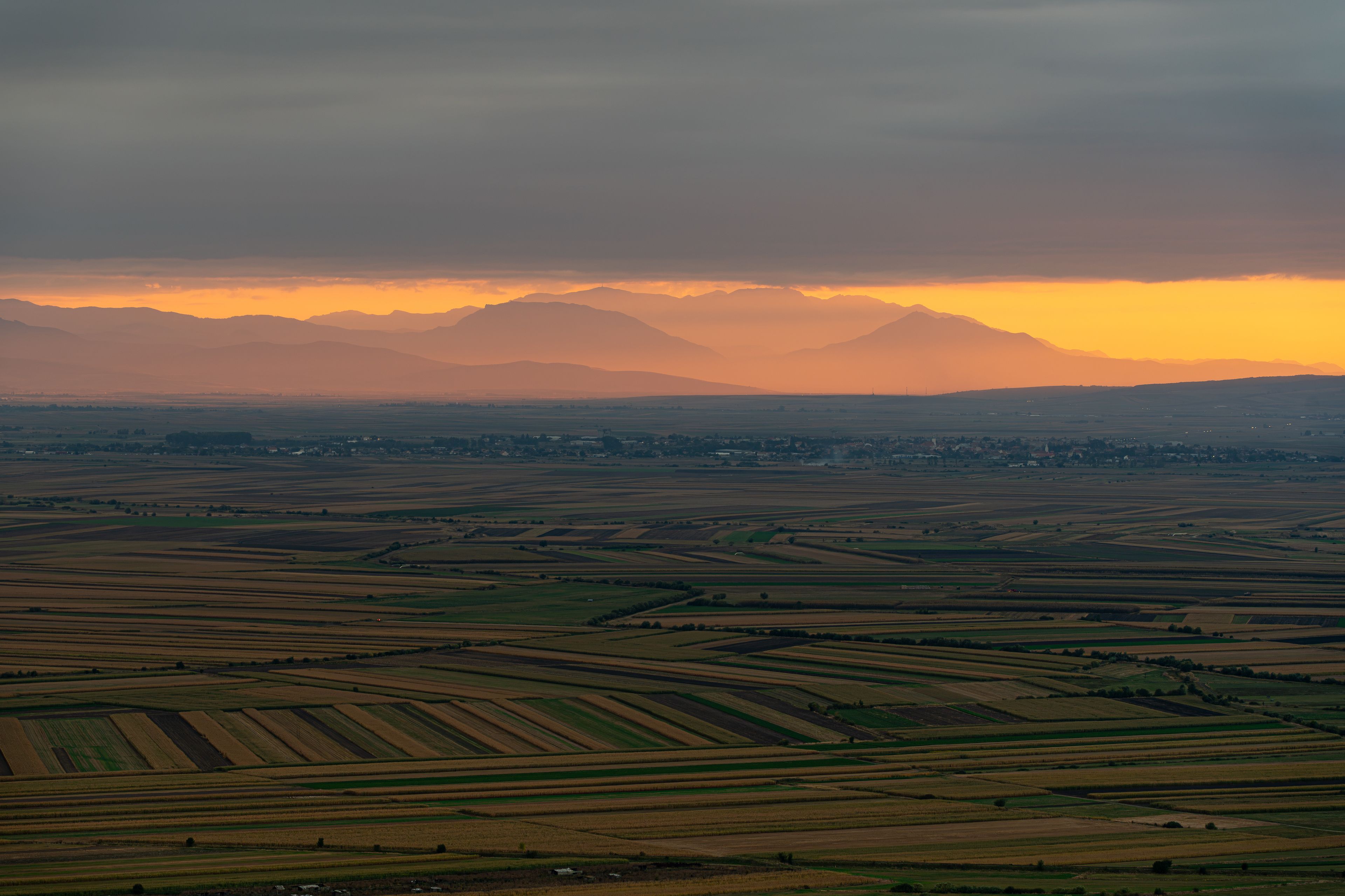 View of the sunset over the agricultural fields and distant mountains in Mereni, Covasna County, Romania.