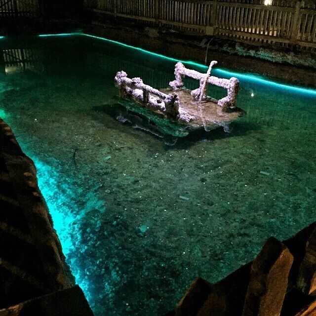 A submerged shipwreck in clear water with a greenish hue, surrounded by rocky terrain.