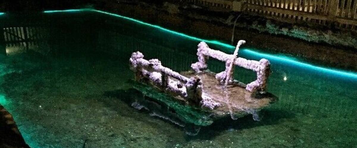 A submerged shipwreck in clear water with a greenish hue, surrounded by rocky terrain.