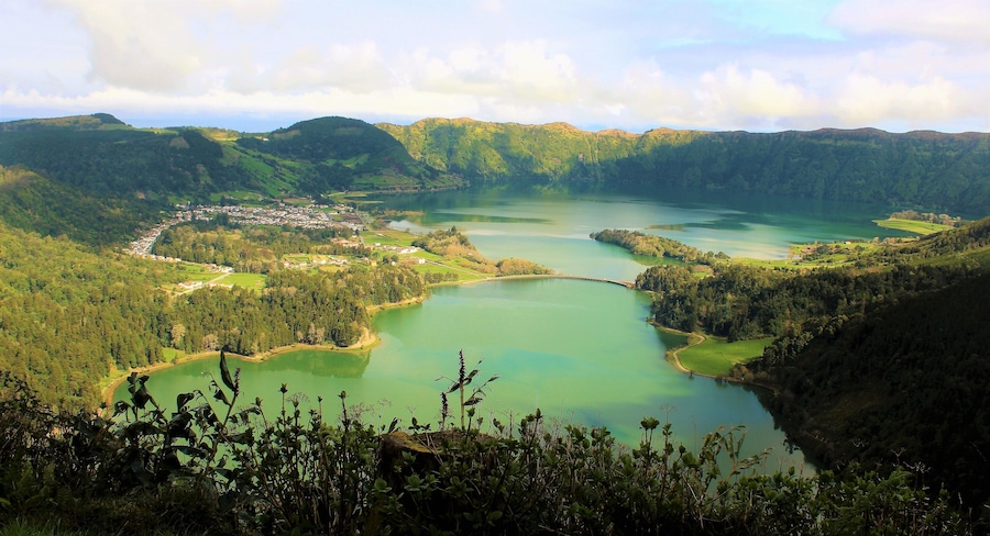 I took this on March 22nd in the Azores Islands, Portugal! It features Lagoa das Sete Cidades (Lagoon of the Seven Cities). This is a twin lake situated in the crater of a dormant volcano. It's one of the Azores' most beautiful and iconic spots! Before the construction of the bridge it was originally one lake. Now it is the "Green Lake" and "Blue Lake". And in the distance you can see the Atlantic Ocean! I actually visited it twice :). On the 2nd day it was much more foggy and cloudy but still very nice!! On both days there was a real feeling of serenity :). I also saw a couple of other lakes similar to this, too. A truly magical green island!!