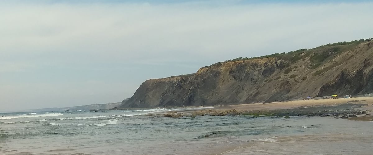 A beach with gentle waves, a sandy shore, and a rocky cliff in the background.
