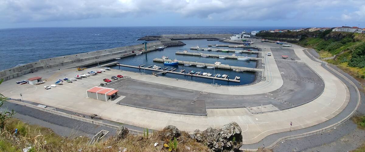 A coastal marina with boats docked, a parking area, and a curved road leading to the water.