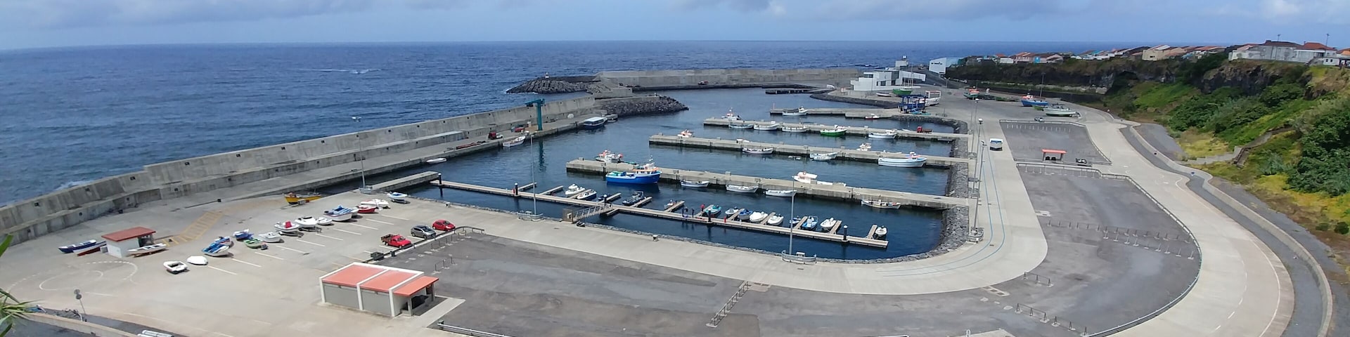 A coastal marina with boats docked, a parking area, and a curved road leading to the water.