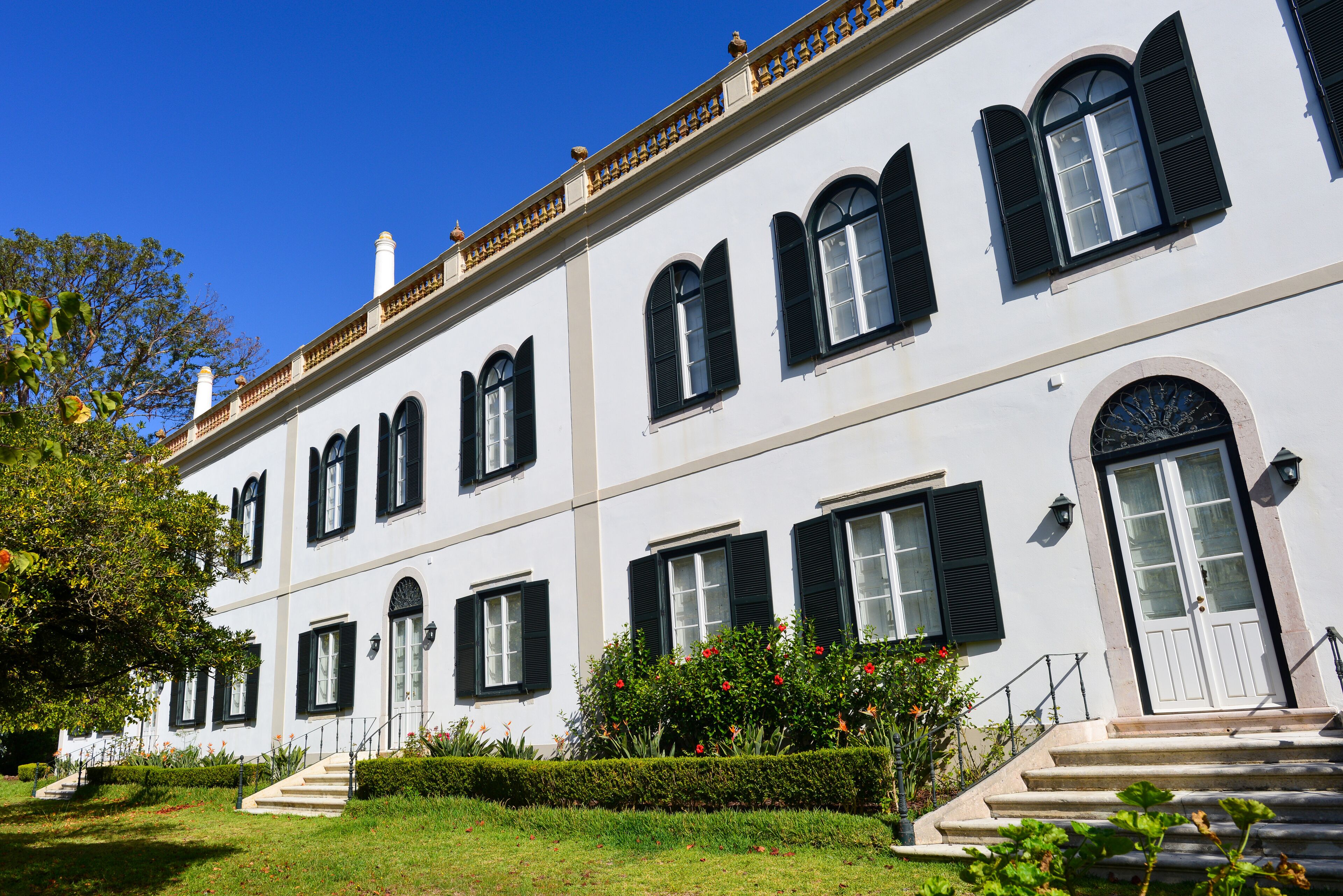 A white building with black shutters, a large arched window, and a staircase leading to the entrance.