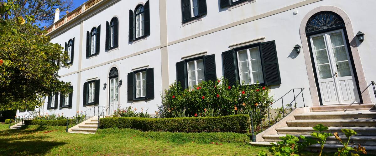 A white building with black shutters, a large arched window, and a staircase leading to the entrance.