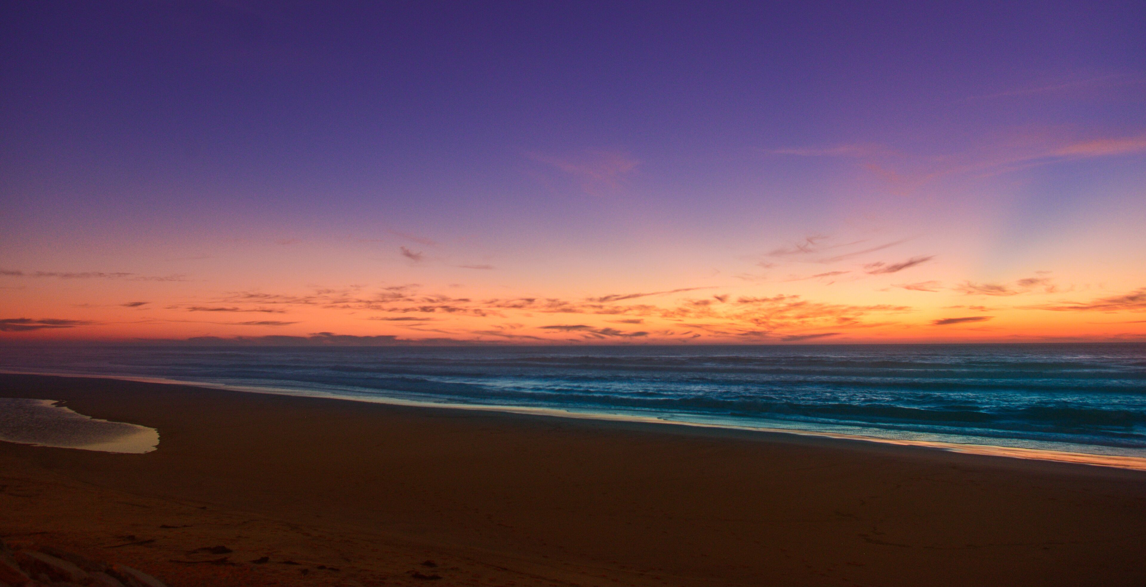 A beach at sunset with a colorful sky and ocean waves.