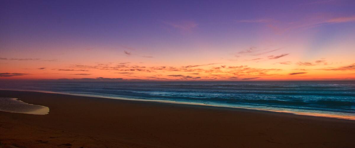 A beach at sunset with a colorful sky and ocean waves.
