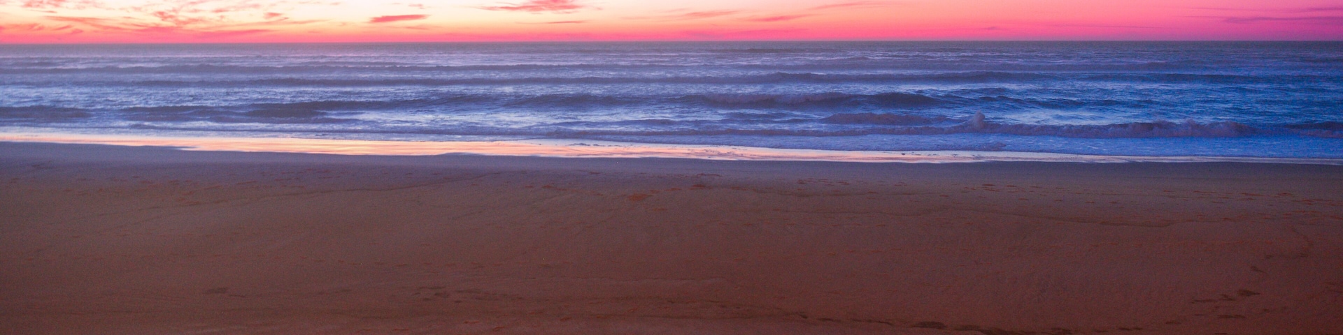 Uma praia com pôr do sol, ondas do oceano e duas cadeiras de madeira.