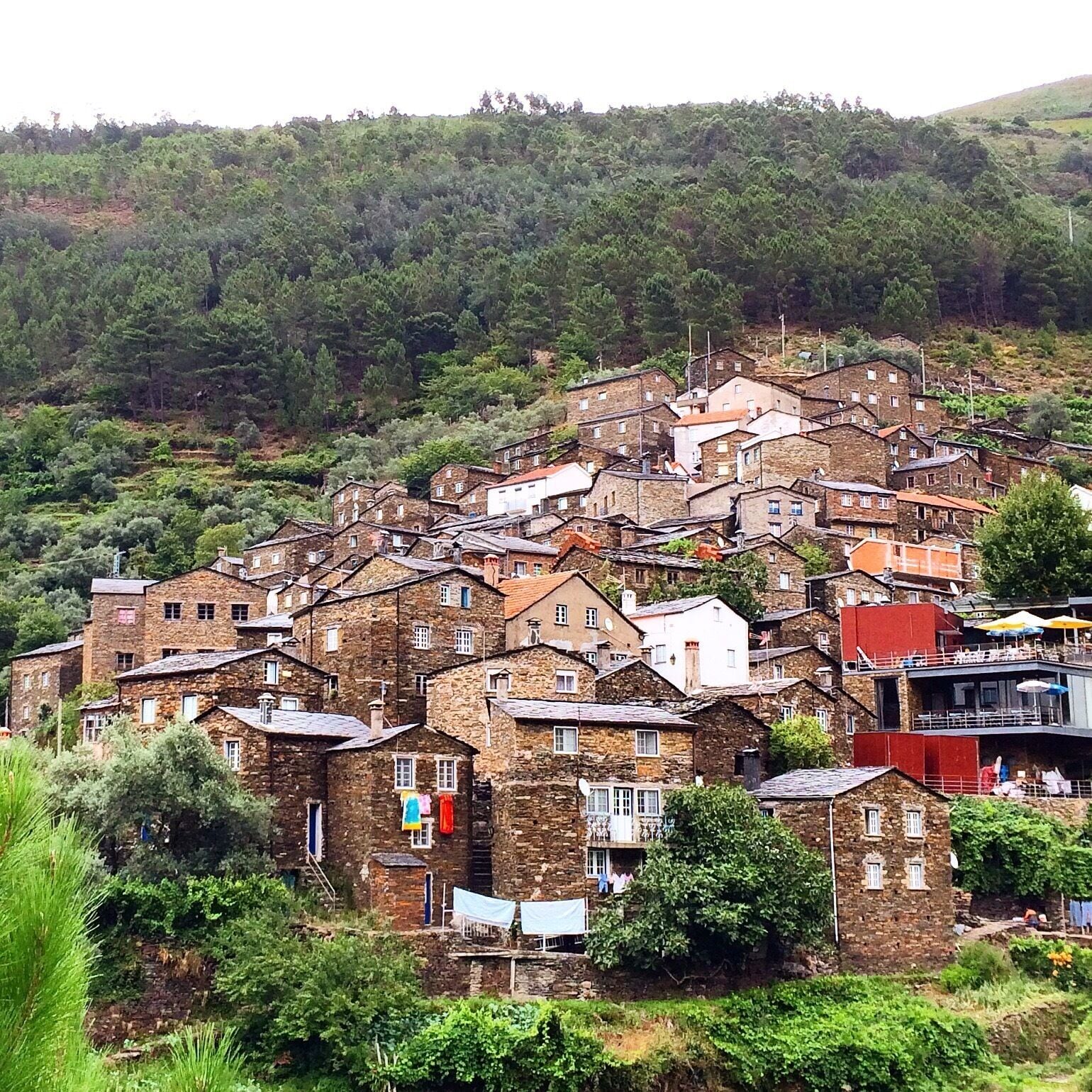 A hillside village with stone buildings and lush greenery.