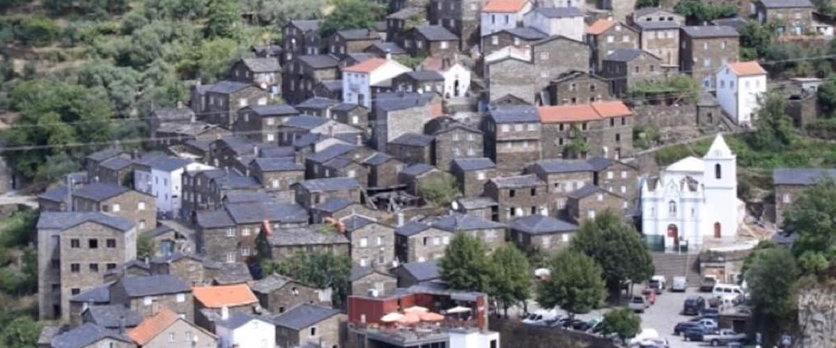 A densely packed hillside village with stone buildings, a prominent church, and a winding road.