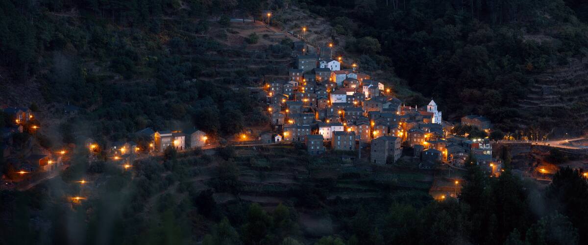 A village nestled in a valley surrounded by forested hills at dusk.